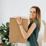 cheerful woman carrying packed carton box